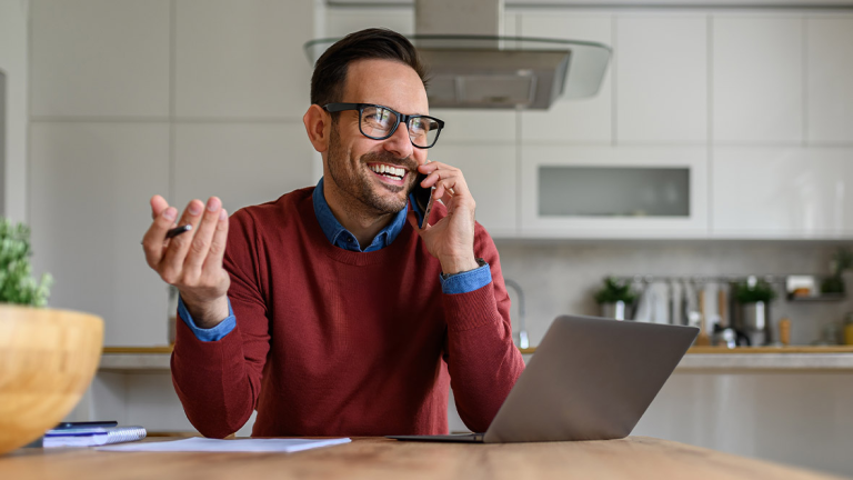 Man talking on his mobile phone at a kitchen bench beside a laptop